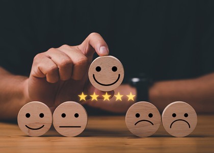 Wooden circle with a smiley face drawn on it and five yellow stars underneath it, being held above four other wooden circles with straight faces, frown faces and less smiley faces drawn on them. 